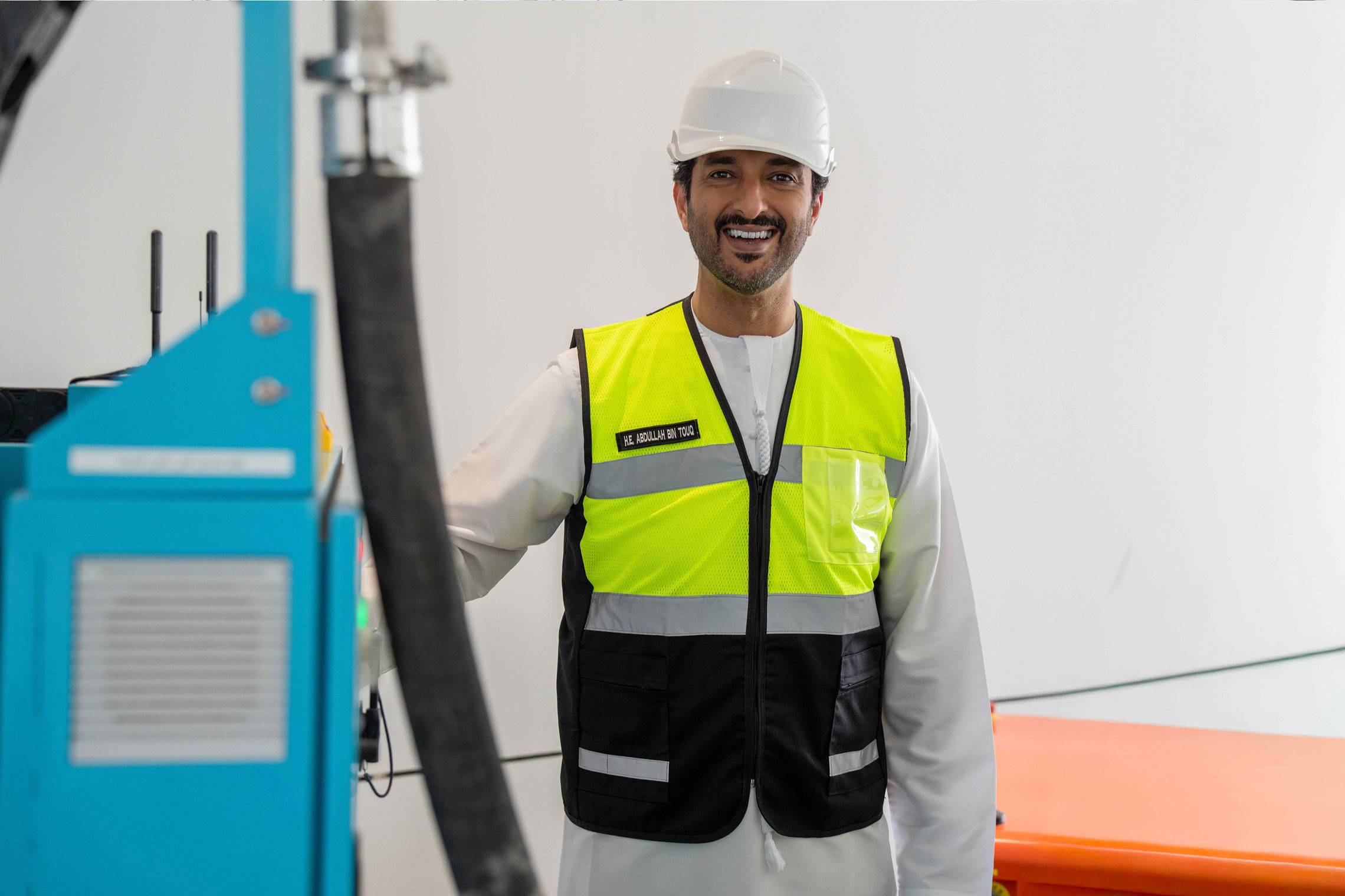 Emirati official in hard hat and hi-vis beside an automated construction robot at Innovo site